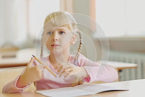 Five years old blonde girl sitting at classroom and writing