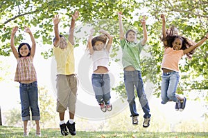 Five young friends jumping outdoors smiling