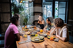 Five young friends sitting at the table in a cafe, chatting, hav