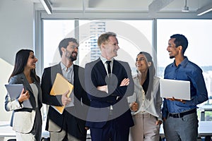 Five young happy professional team business people standing in office laughing.