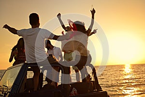 Five young people having fun in convertible car at the beach at sunset.