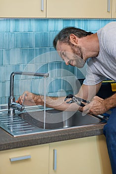 Fixing leaky faucet. Professional plumber looking concentrated, using pipe wrench while examining and fixing faucet in