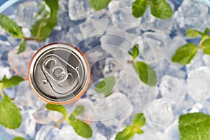 Fizzy drink in a aluminium tin can on the background of ice cubes and fresh mint leaves. Top view.