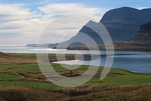 Fjord with green field, sea, mountains and blue sky in the background