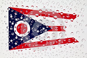 Flag of American State Ohio behind a glass covered with rain drops.