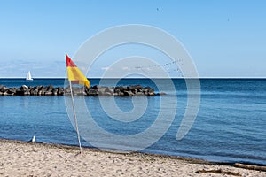 A flag on the beach. Seascape, sky and seagulls. Rock Sail on the horizon.