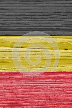 The flag of Belgium on dry cracked wooden surface. It seems to flutter in the wind. Faded paint. Vertical background or backdrop