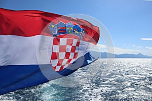 The flag of Croatia flutters in the wind against the background of the sea and the sky, close-up