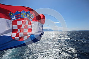 Flag of Croatia over the sea against the backdrop of the sea coast, mountains on the horizon, blue sunny sky