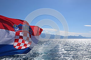 Flag of Croatia over the sea against the background of a blue sunny sky, mountains on the horizon