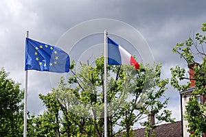 Flag of EU, european union and France, tricolor red white blue colors, fluttering, waving on flagpole in wind against sky and