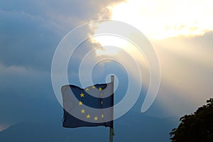 The flag of the european union flies in the wind against the backdrop of mountains at sunset