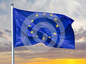 Flag of the European Union waving in the wind on flagpole against background of the sunrise