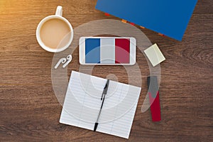 flag of France on a smartphone on a wooden table, notebook and pen, textbook,