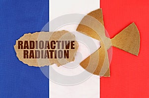 On the flag of France, the symbol of radioactivity and torn cardboard with the inscription - Radioactive Radiation