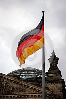 The flag of Germany flutters proudly near the German Parliament building against a cloudy sky