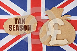 On the flag of Great Britain, a bag with a money symbol and a cardboard with the inscription - TAX SEASON