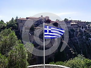 Flag of Greece is displayed against background of ancient monastery located on impregnable rock.