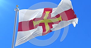 Flag of Guernsey waving at wind in slow in blue sky, loop