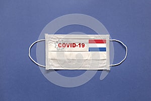 The flag of Holland and inscription COVID-19 on a medical mask on a blue background. Healthcare and medical concept. Pandemic