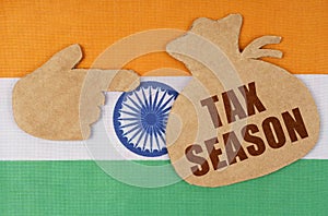 On the flag of India, cardboard figures of a hand and a money bag with the inscription - TAX SEASON