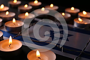 Flag of Israel, barbed wire and burning candles on black background. Holocaust memory day