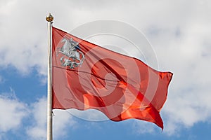 Flag of the Moscow region on the pole against the background of the cloudy sky, close-up. Red banner with the image of