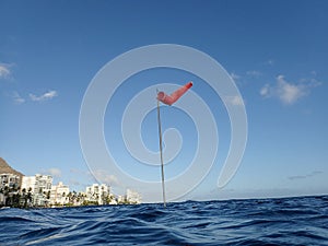 Flag pole with wind sock rises above the wavy waters of Waikiki