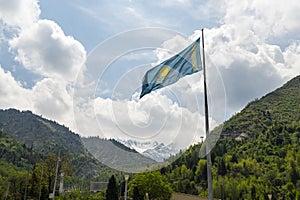 The flag of the Republic of Kazakhstan on top of a mountain, against a background of blue sky with white clouds