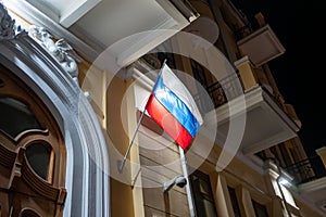 flag of Russian Federation develops in wind at night on administrative building.