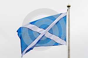 Flag of Scotland Saltire or the Saint Andrew`s Cross blowing in the wind towards cloudy grey sky in a rainy day