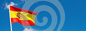 Flag of Spain waving in the wind on flagpole against the sky with clouds on sunny day