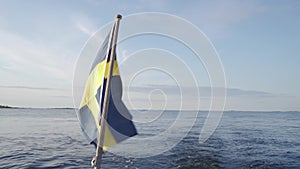 Flag of Sweden on the back of a boat, blowing in the wind while sailing at sea.