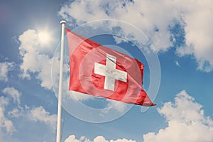 Flag of Switzerland, National symbol waving against cloudy, blue sky, sunny day