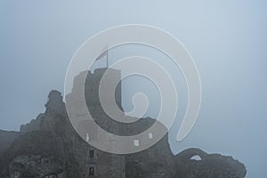 Flag on top of medieval castle ruin in heavy fog