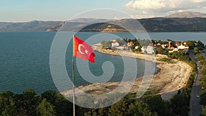 The flag of Turkey is fluttering in the wind among the beautiful landscape of turkish nature with Egirdir lake