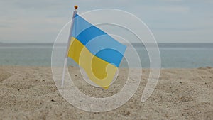 Flag of Ukraine, standing in the sand, against the background of the sea.