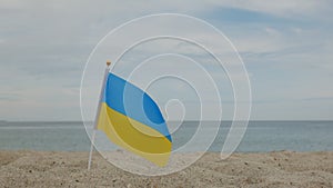 Flag of Ukraine, standing in the sand, against the background of the sea.