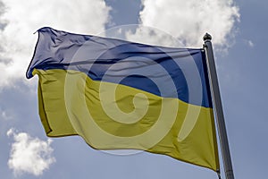 Flag of Ukraine waving in the wind on flagpole against the sky with clouds on sunny day