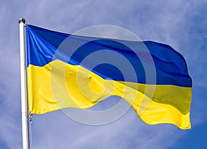 Flag of Ukraine waving in the wind on flagpole against the sky with clouds on sunny day