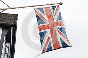 Flag of United Kingdom the Union Jack also known as Union flag blowing in the wind in front of an old traditional timber house,