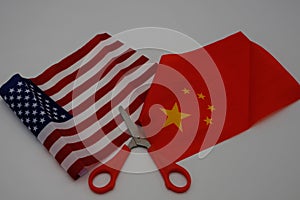A flag of the United States of America with another of China and with a scissor in the middle that cuts