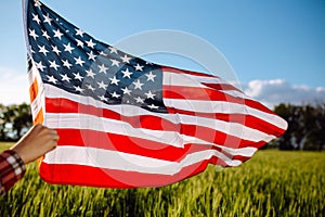 Flag of United States of America flies on the wind. Boy walking with the american flag on the green wheat field