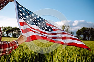 Flag of United States of America flies on the wind. Boy walking with the american flag on the green wheat field celebrating