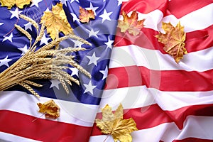 Flag United States America strewn with yellowed autumn maple leaves and bunch wheat ears.