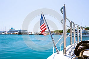 The flag of the United States flutters in the wind on a stainless steel flagpole at the stern of a motor yacht. Marina in the port