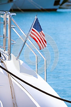 The flag of the United States flutters in the wind on a stainless steel flagpole at the stern of a motor yacht. Marina in the port