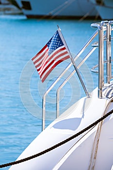 The flag of the United States flutters in the wind on a stainless steel flagpole at the stern of a motor yacht. Marina in the port