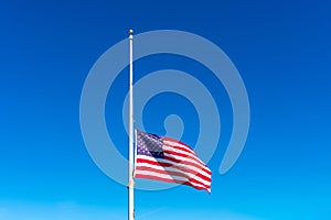 Flag of the United States flying at half staff waving in the wind under blue sky