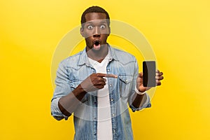 Flagman gadget. Portrait of amazed man pointing at cellphone. indoor studio shot isolated on yellow background
